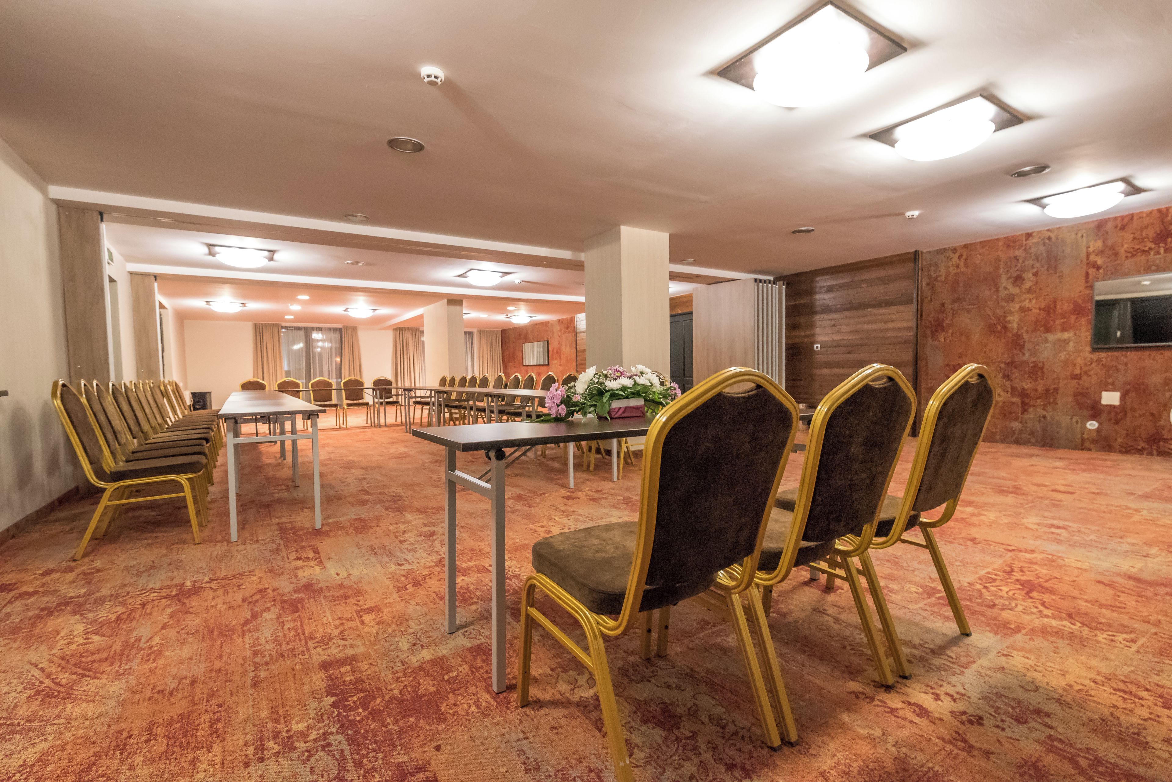 Un salón de conferencias con una larga mesa, sillas, piso alfombrado e iluminación en el techo.