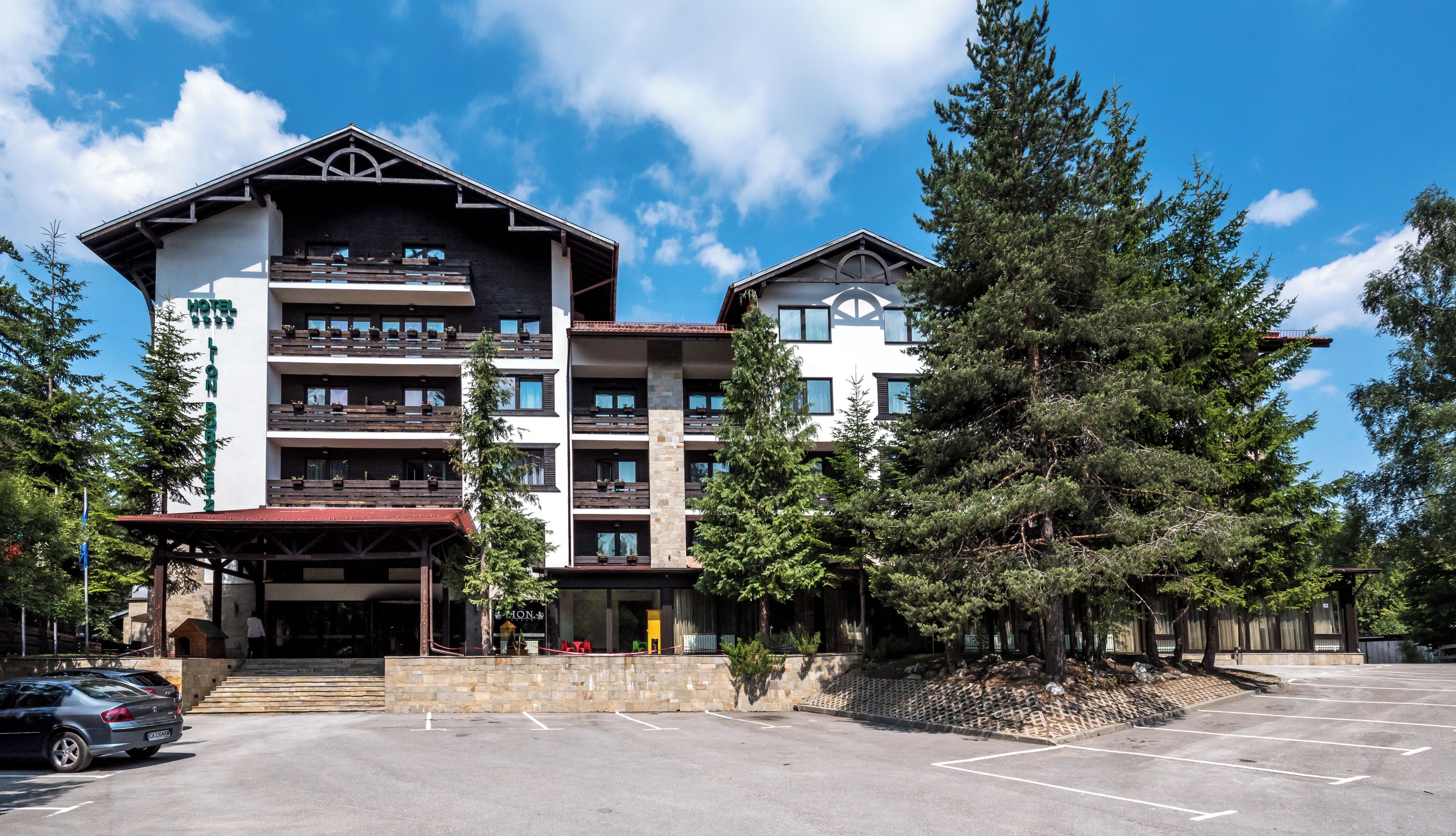 A multi-story hotel with a covered entrance, outdoor seating, and a parking lot.