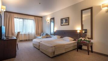 Habitación de hotel con una cama doble, un escritorio con silla, un televisor y un ventanal con cortinas.