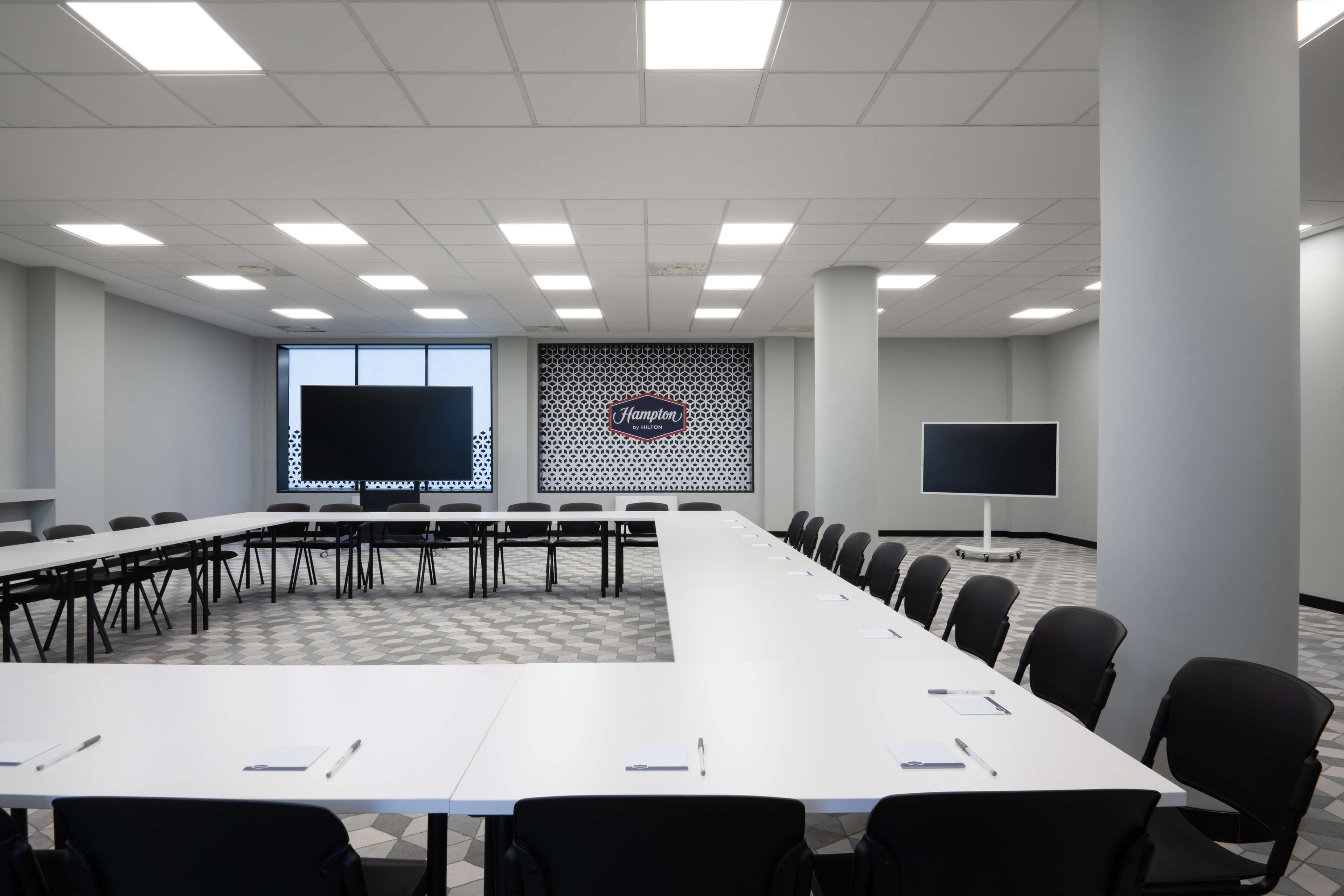 A conference room with a long table, chairs, a large screen, and a patterned wall.