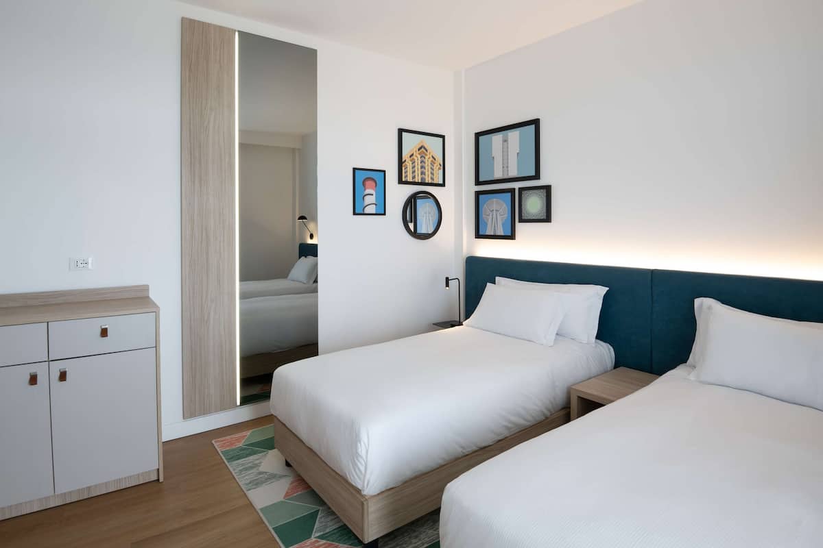 A hotel room with two single beds, a wardrobe, and a mirror on the wall.