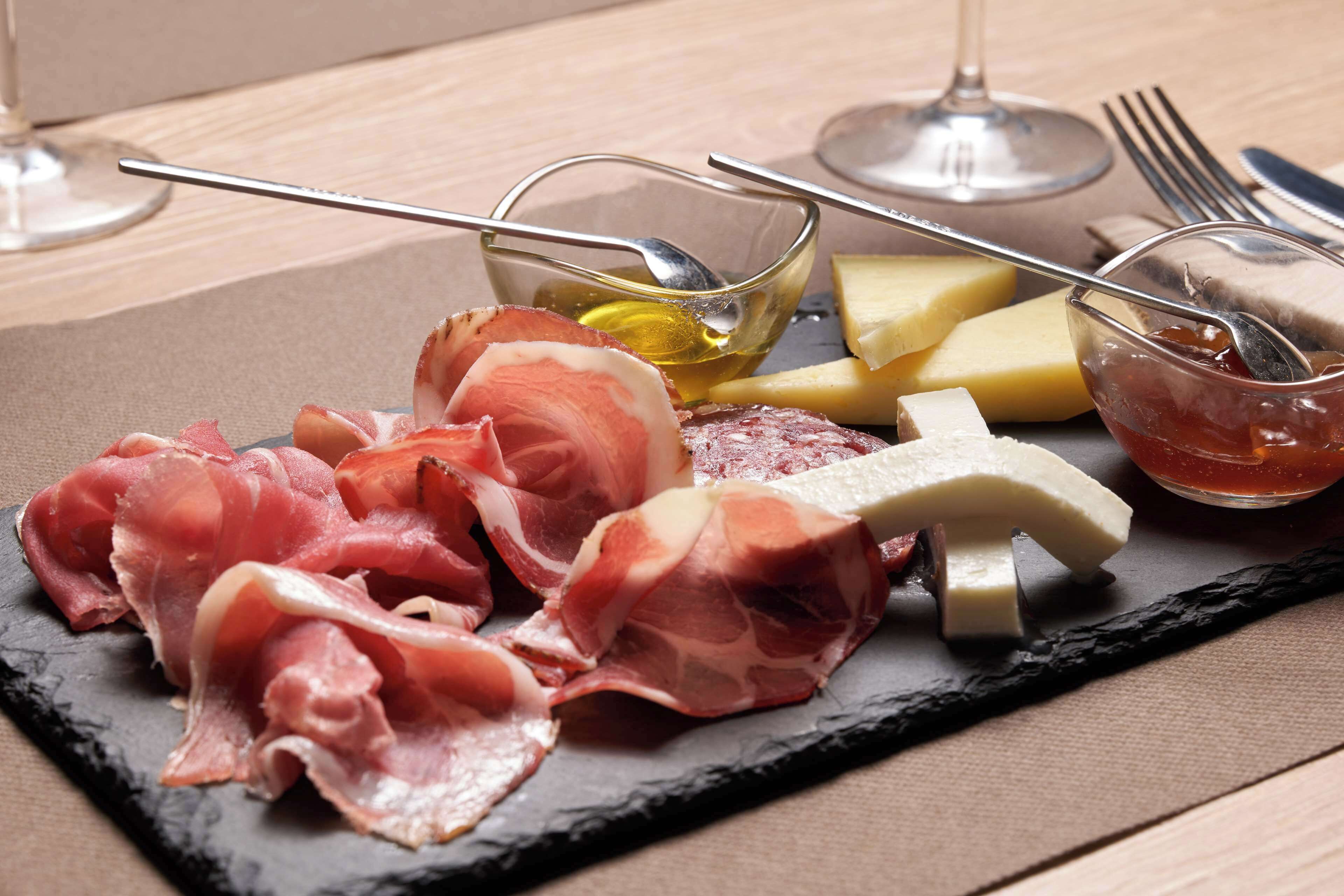 Une planche de charcuterie comprenant divers types de viandes, de fromages et de condiments, le tout présenté sur une ardoise.