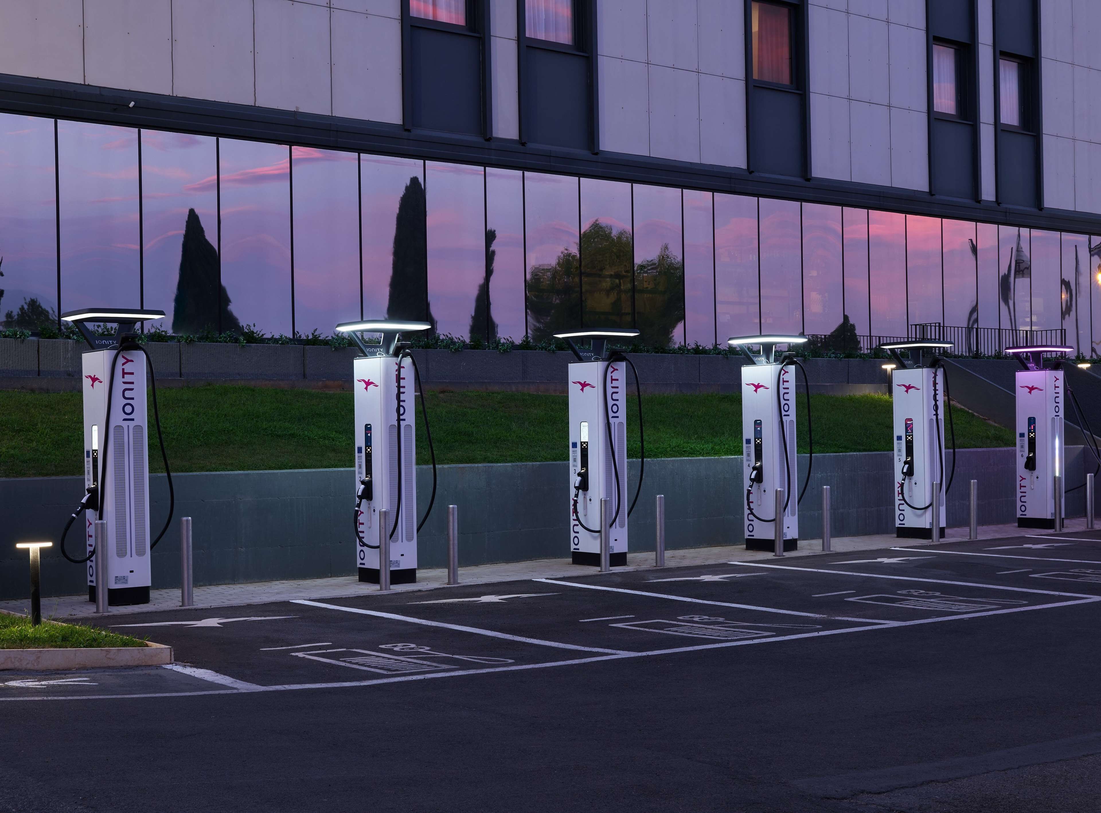 A row of electric vehicle charging stations with a modern building in the background.