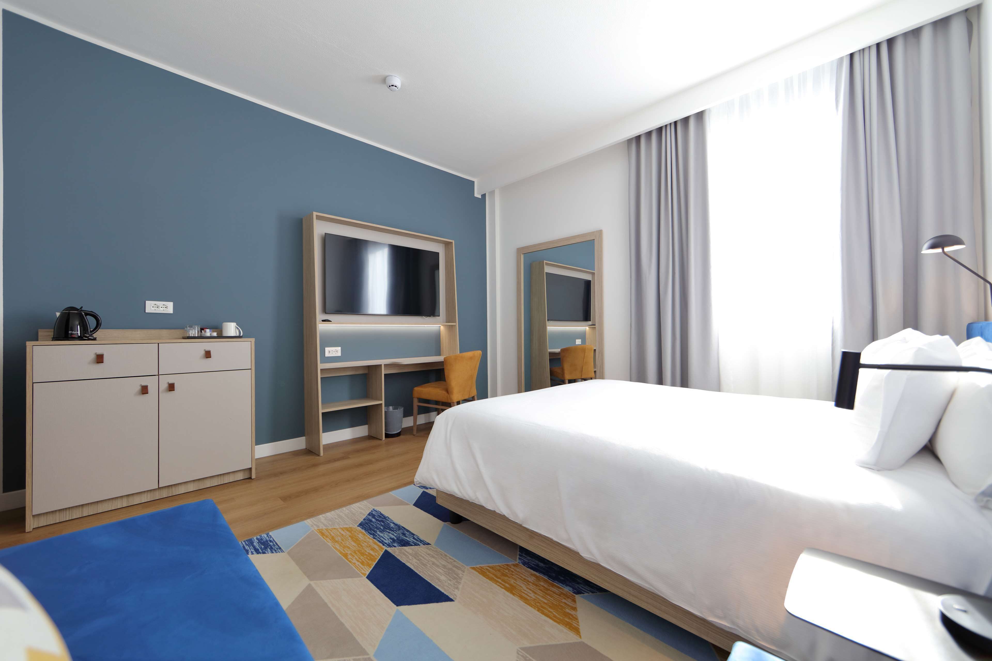 Habitación de hotel con una cama grande, un escritorio con silla, un armario y un espejo.