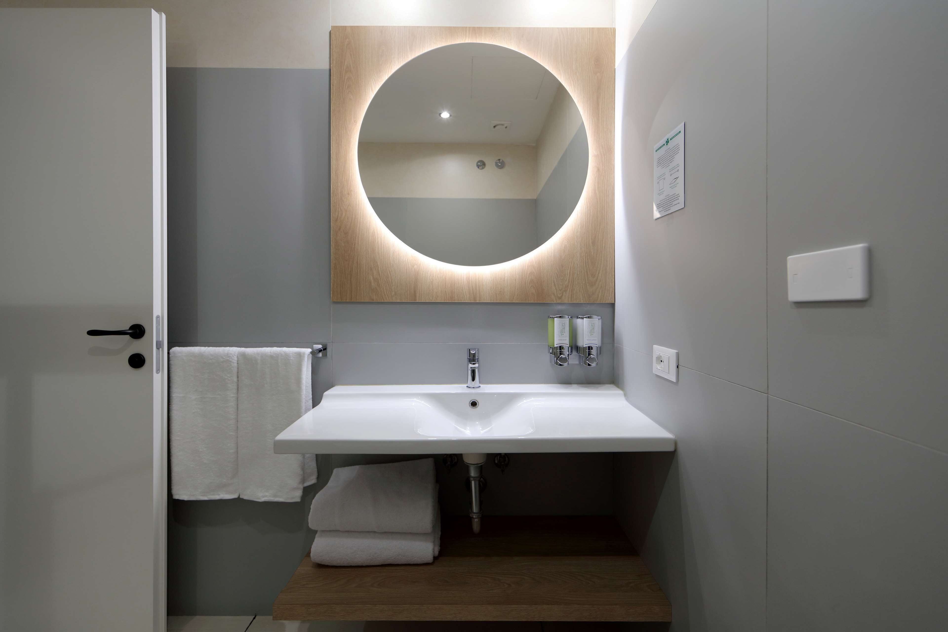 A modern bathroom with a large mirror, white sink, and a towel rack.