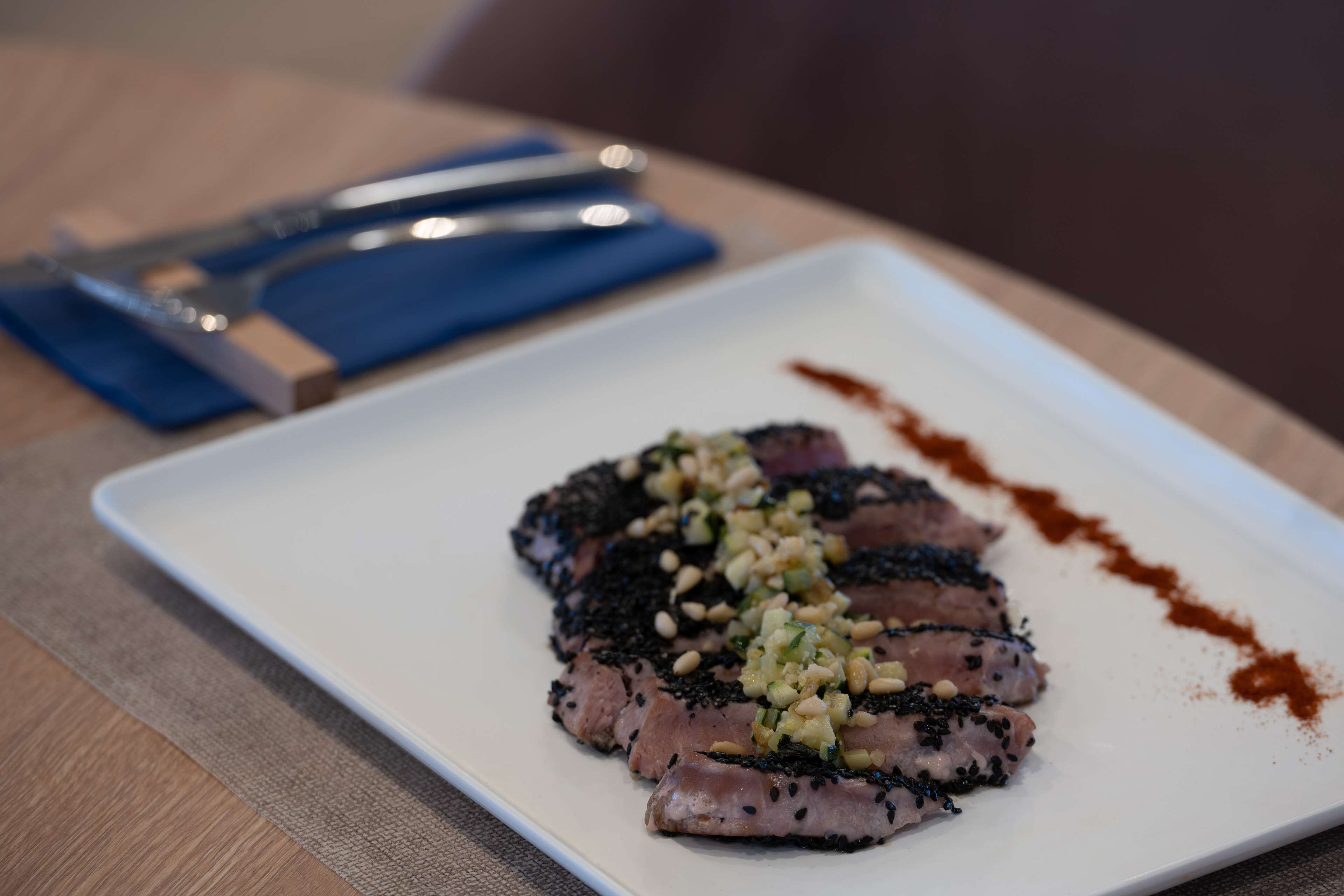 A white plate with sliced meat, black sesame seeds, and a garnish on a wooden table.