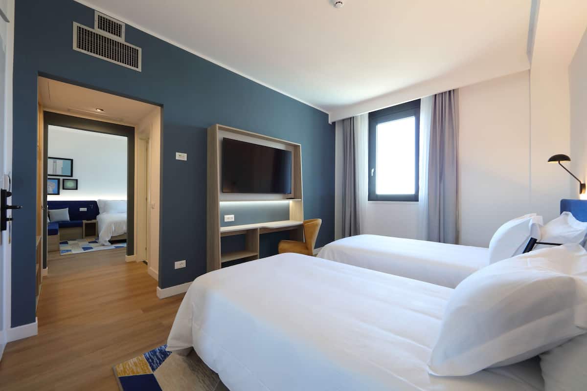 A hotel room with two beds, a TV, and a desk.