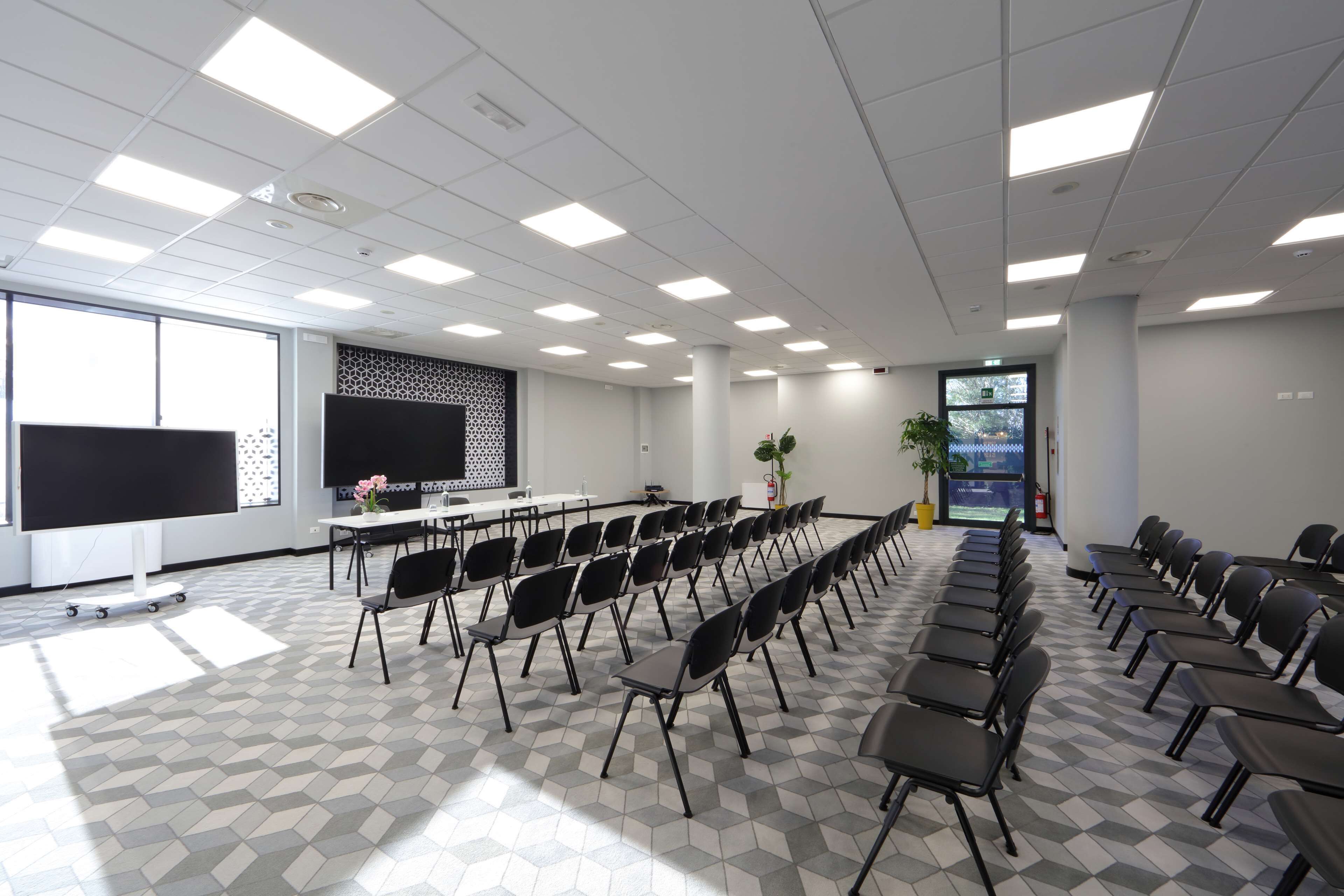 A conference room with a long table, rows of chairs, a projector screen, and a patterned floor.