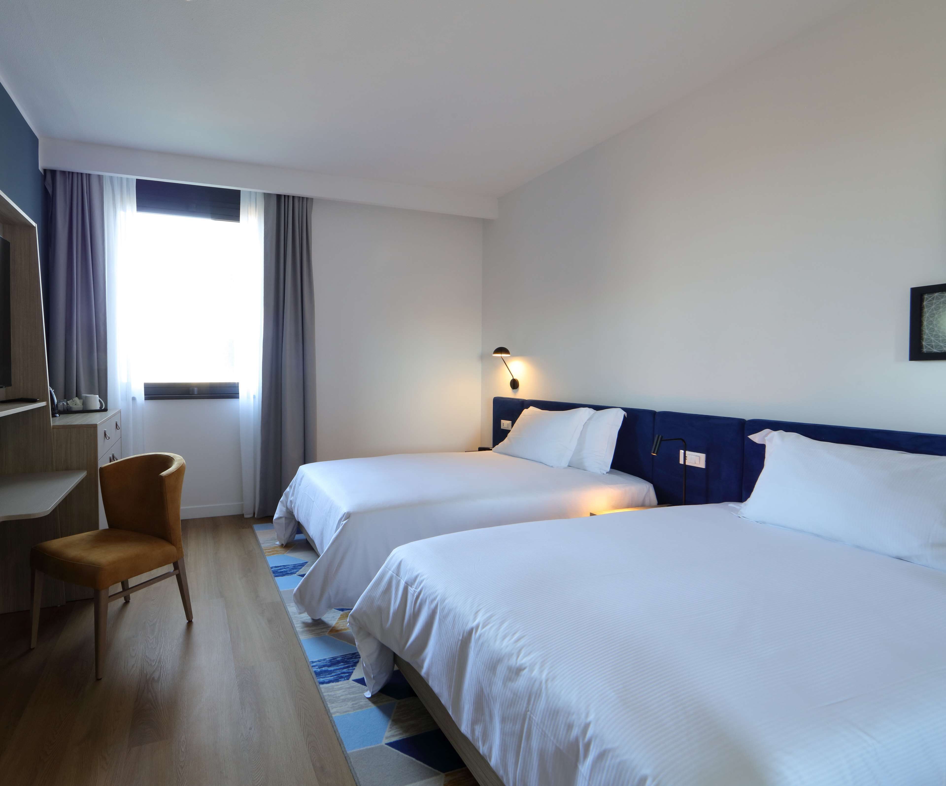 Una camera d'albergo con due letti, una scrivania, una sedia e una finestra con tende.