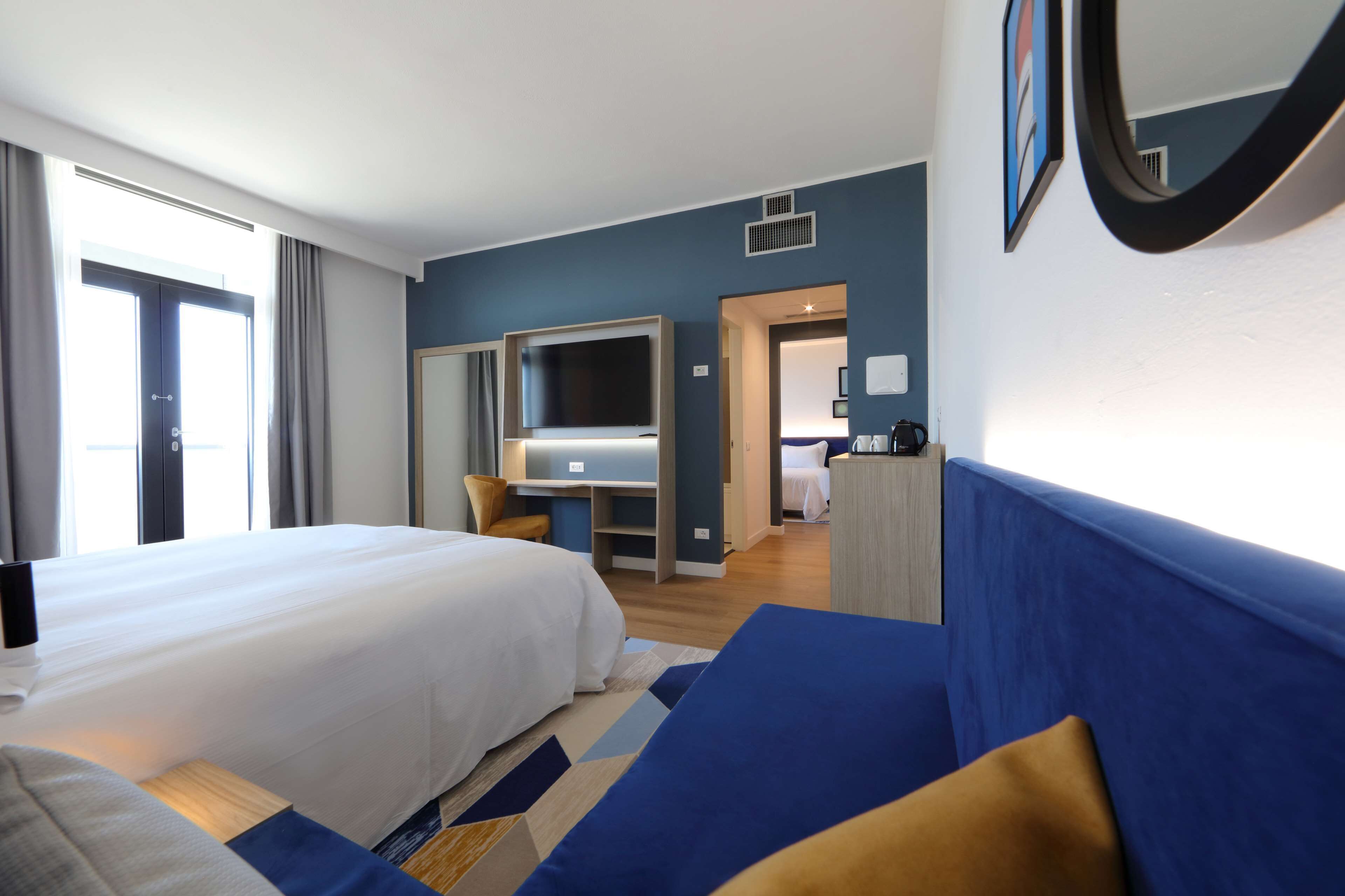 Une chambre d’hôtel avec un grand lit, un bureau, une armoire et une salle de bain visible à travers une porte ouverte.