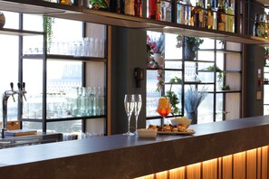 A bar area with a counter, shelves with bottles, a window with a view, and a decorative plant.