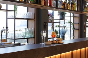 Una zona de bar con mostrador, estanterías llenas de botellas, una ventana con vistas y una planta decorativa.