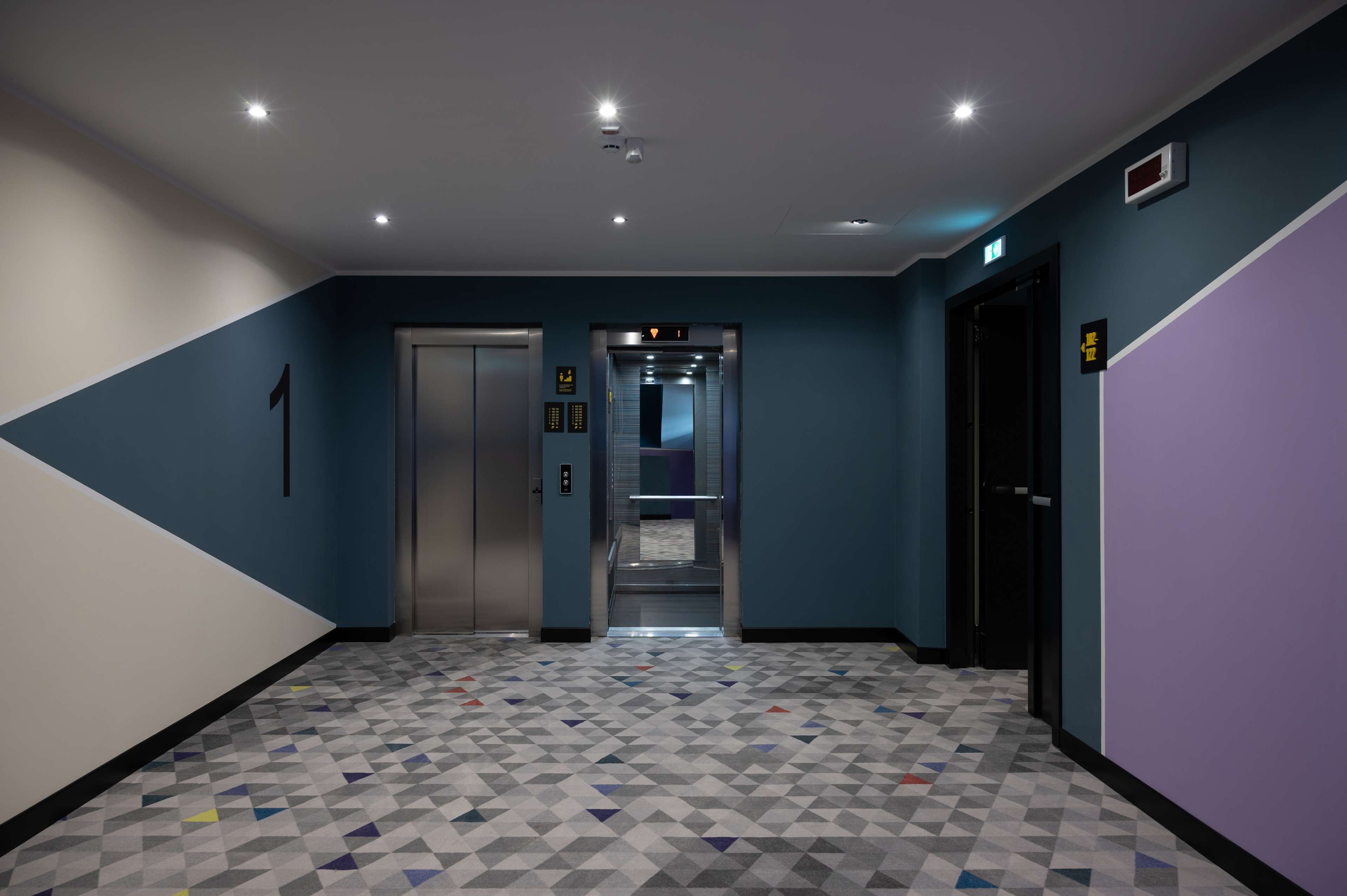 Un pasillo con piso de diseño geométrico, un ascensor y una puerta con el símbolo de número.