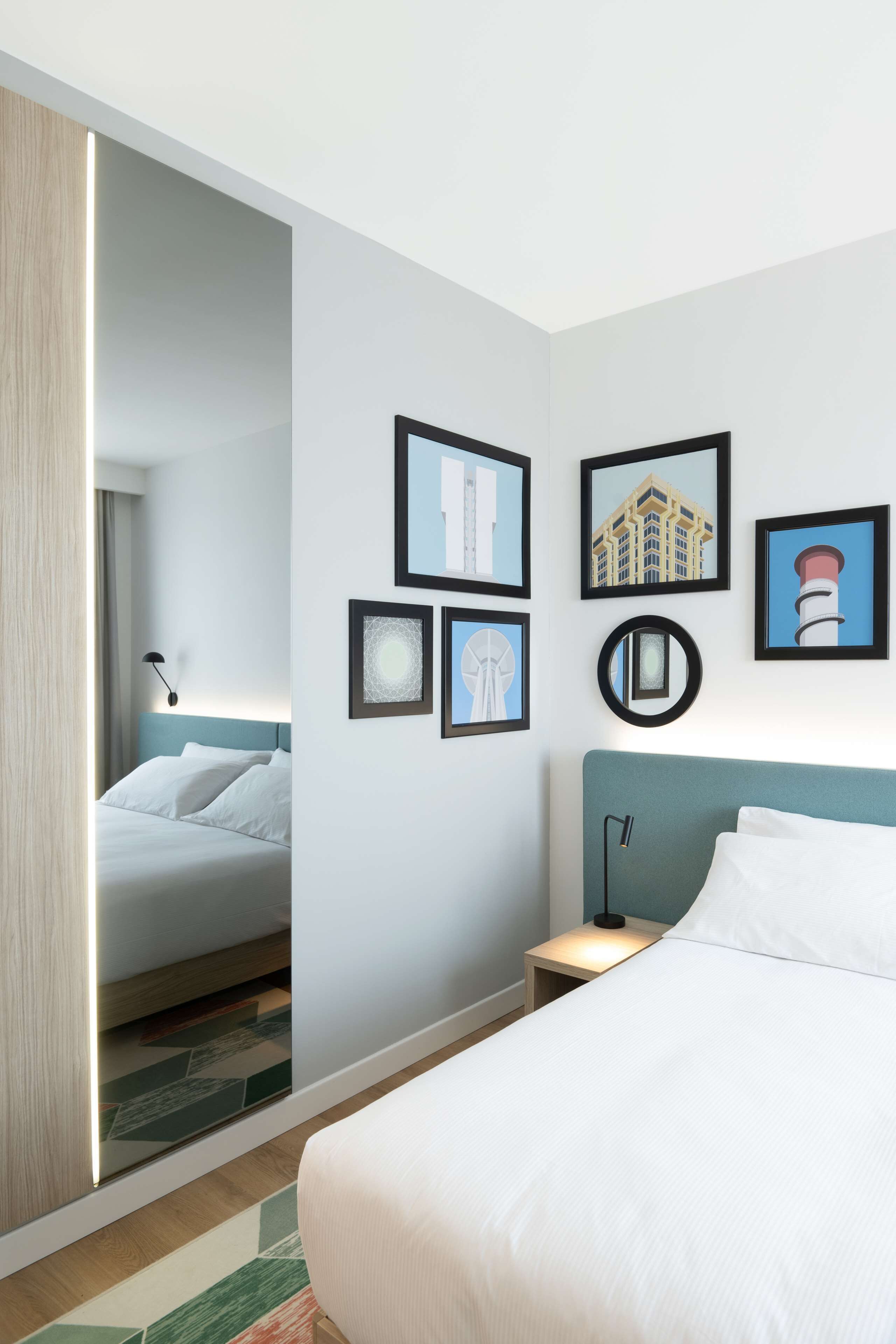 A hotel room with a bed, a nightstand, and a wall with framed pictures.