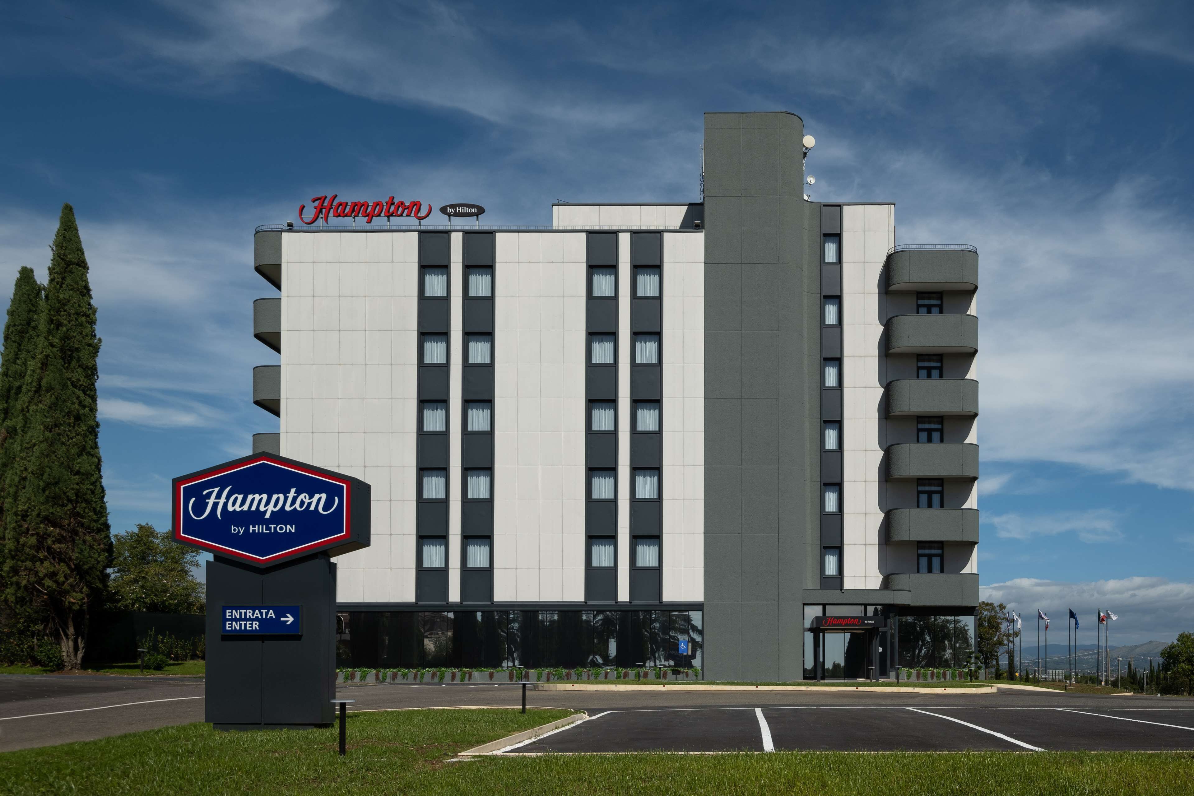 A Hampton by Hilton hotel with a modern design, featuring a prominent entrance and a parking lot.