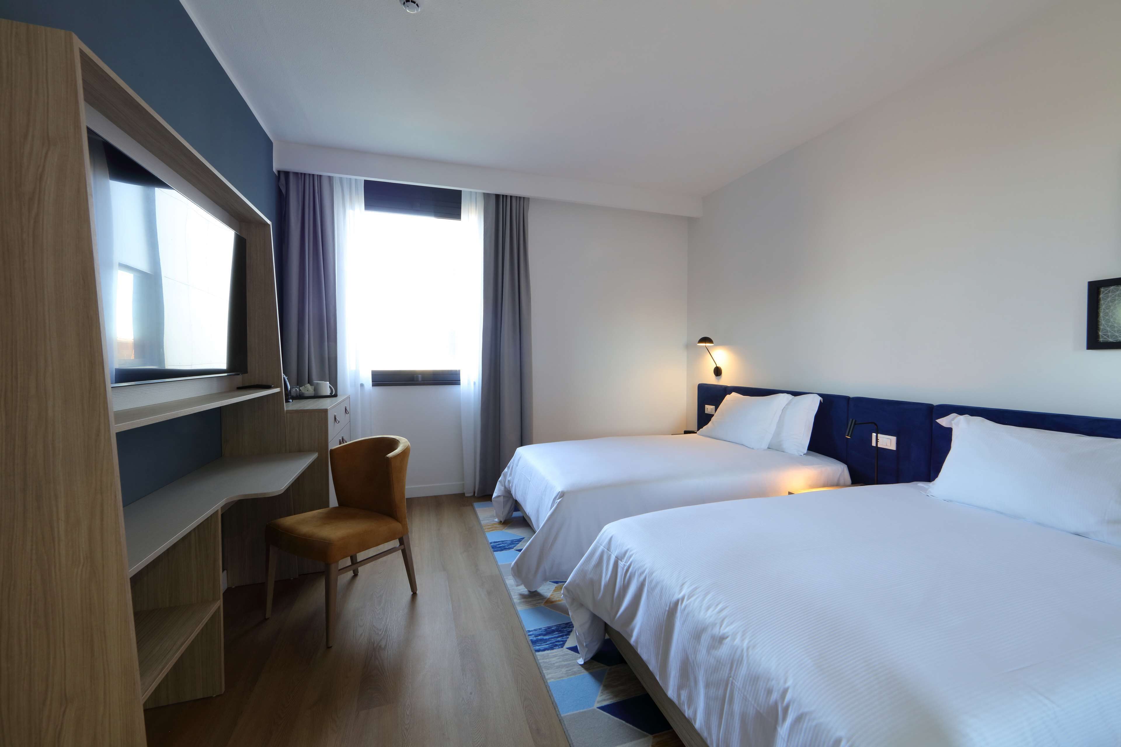 A hotel room with two beds, a desk, and a chair.
