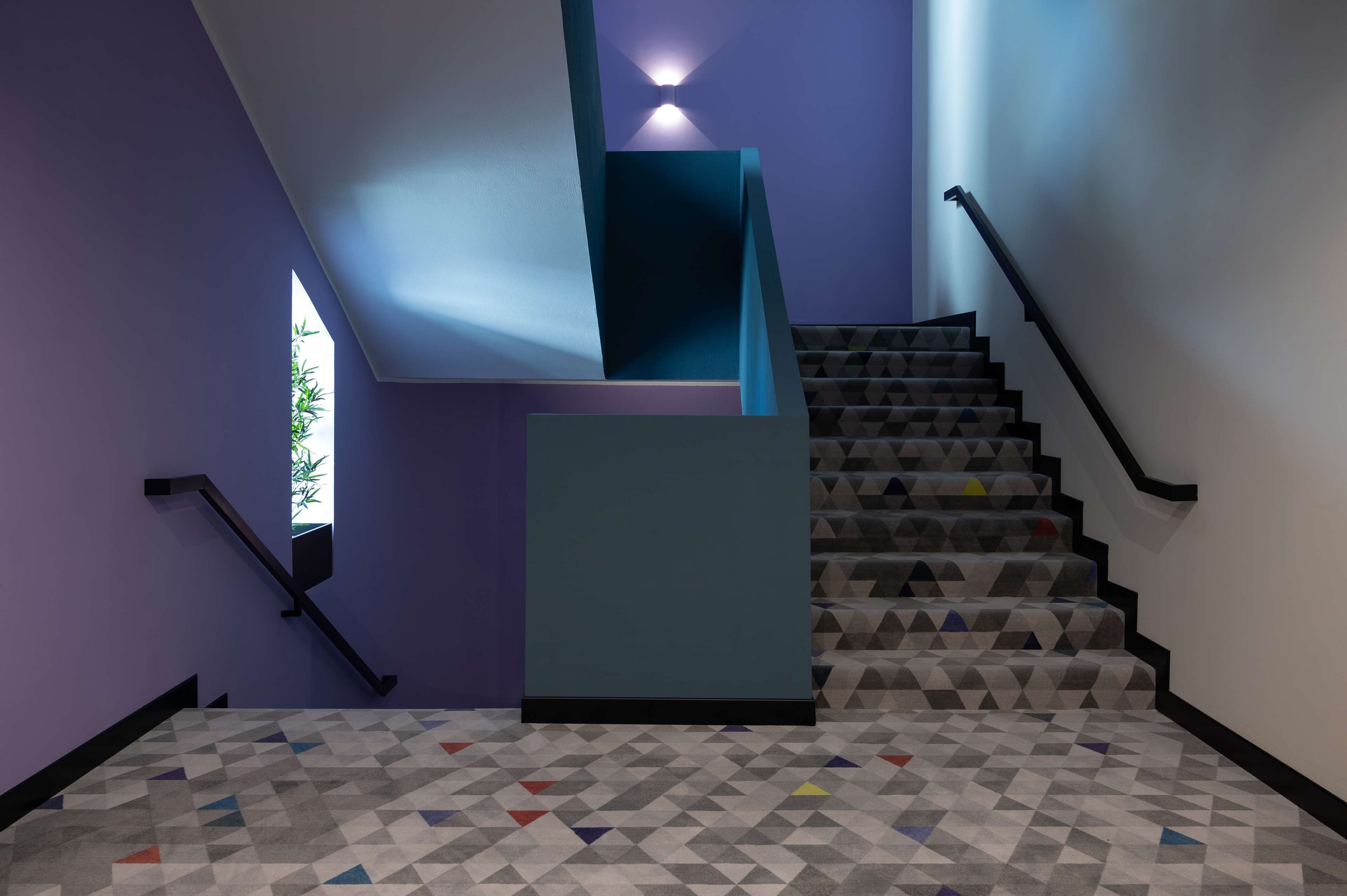 A modern staircase with geometric patterned carpet, a teal accent wall, and a window with natural light.