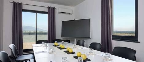 Une salle de conférence équipée d’une grande table, de chaises, d’un écran de projection et offrant une vue sur le paysage grâce à de grandes fenêtres.