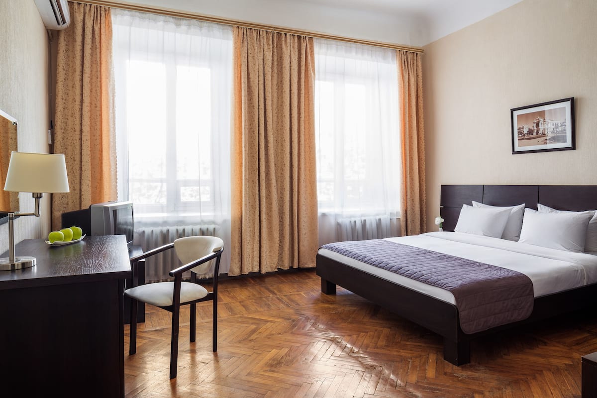 Una habitación de hotel con una cama, un escritorio con lámpara, una silla y una ventana con cortinas.