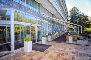 Un edificio moderno con grandes puertas de vidrio, asientos al aire libre y plantas en macetas.