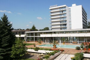 Un hotel moderno con piscina, asientos al aire libre y un edificio grande con balcones.