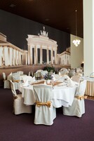 Un salón de banquetes con mesas redondas, manteles blancos y sillas adornadas con cintas doradas.
