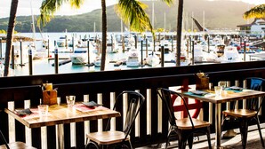 Restaurante con vista a un puerto deportivo. Mesas dispuestas con menús y vasos.