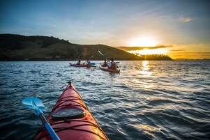 Un kayak sobre aguas tranquilas con un atardecer de fondo.