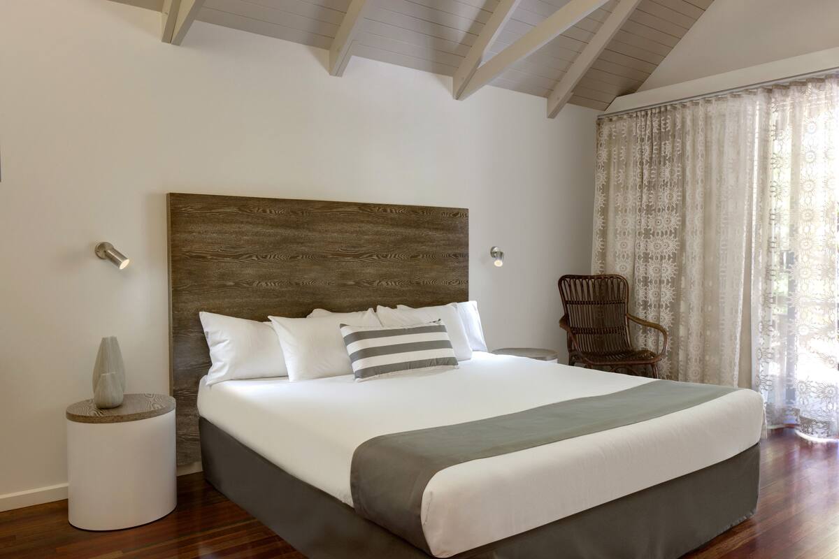 Una cama bien hecha con cabecera de madera, una lámpara de noche y una silla.