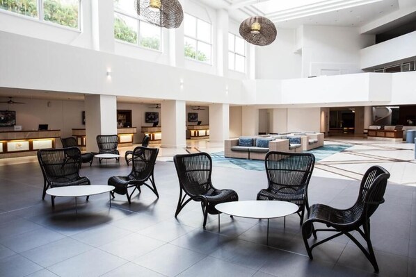 A spacious lobby with high ceilings, large windows, and a central seating area with black wicker chairs and tables. - Palm Bungalows (Whitsundays)