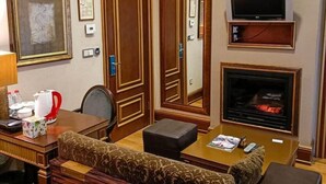 A hotel room with a wooden door, a television, a fireplace, a sofa, a table with a kettle, and framed artwork on the wall. - Sultan Inn Boutique (Baku)