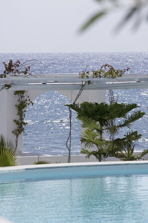 A pool with a view of the ocean, surrounded by greenery and a white structure. - Thalassa Seaside Resort & Suites (Santorini)