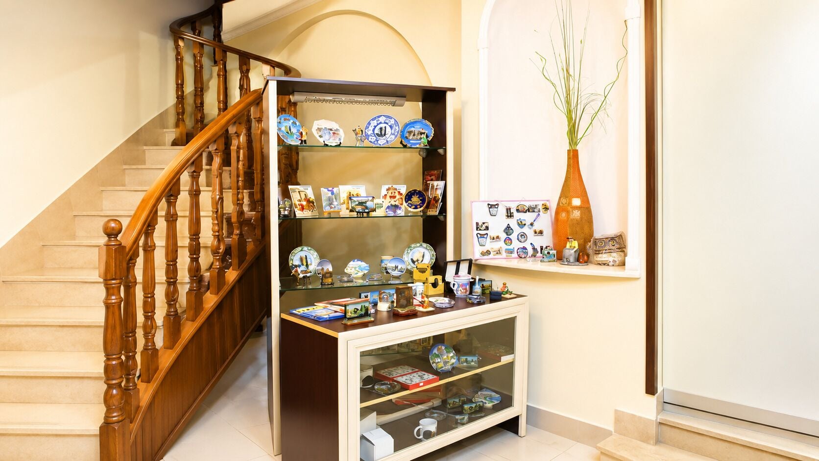 Un escalier avec des balustrades en bois, une vitrine en verre contenant des objets en céramique et une étagère murale ornée d’assiettes décoratives.
