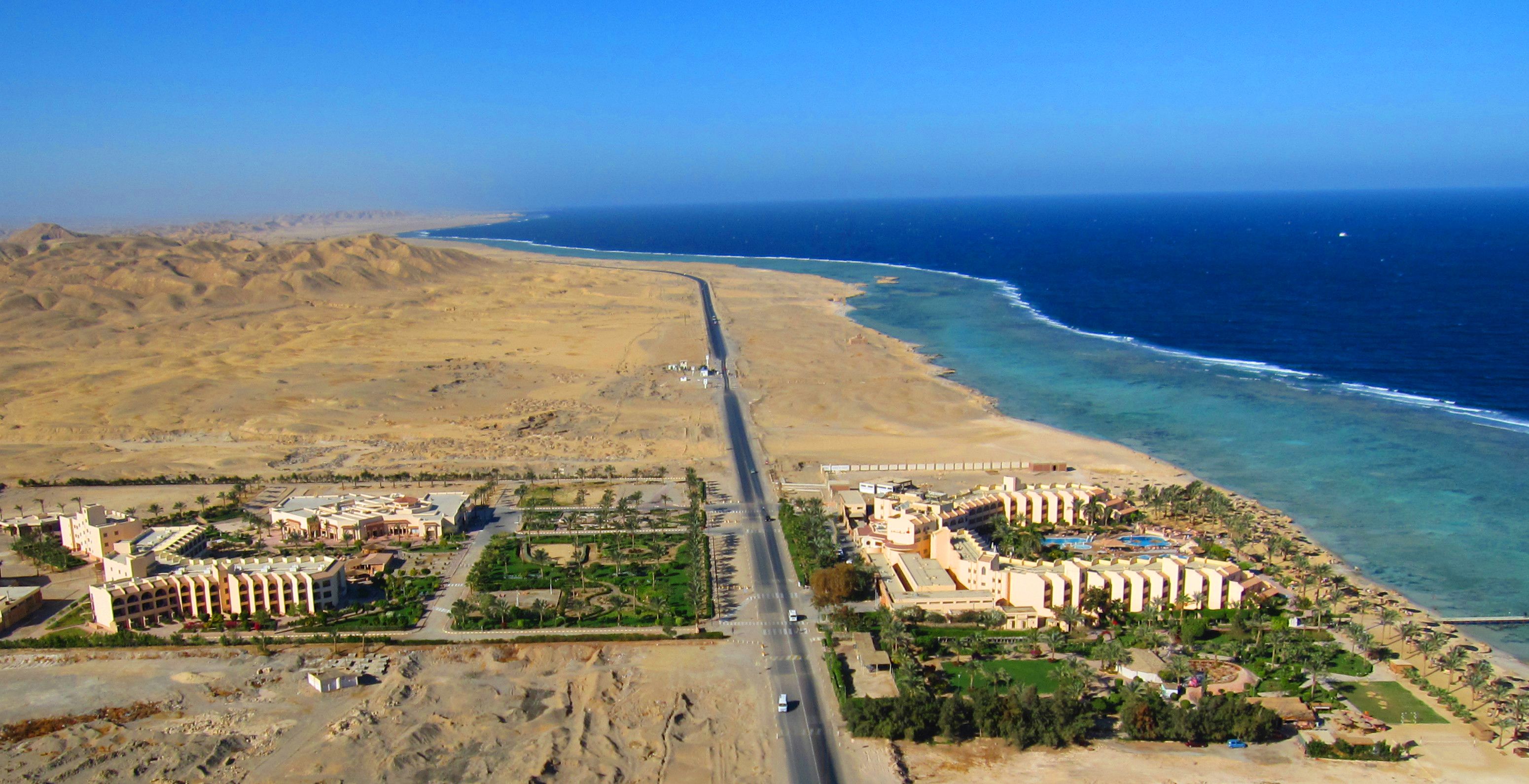 An aerial view of a coastal resort with multiple hotel buildings, a sandy beach, and a clear blue ocean.
