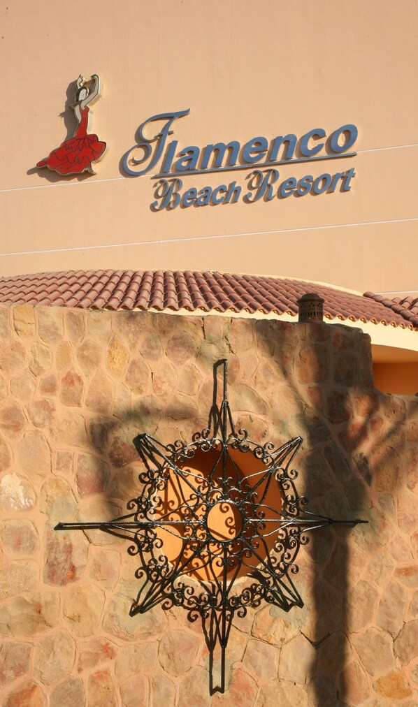 A sign for Flamenco Beach Resort with a decorative metal star and a logo featuring a woman in a red dress.
