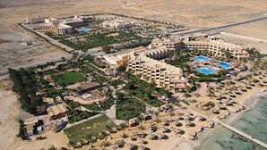Oversigtsbillede af et resort med flere bygninger, et strandareal med liggestole og parasoller, samt en swimmingpool.