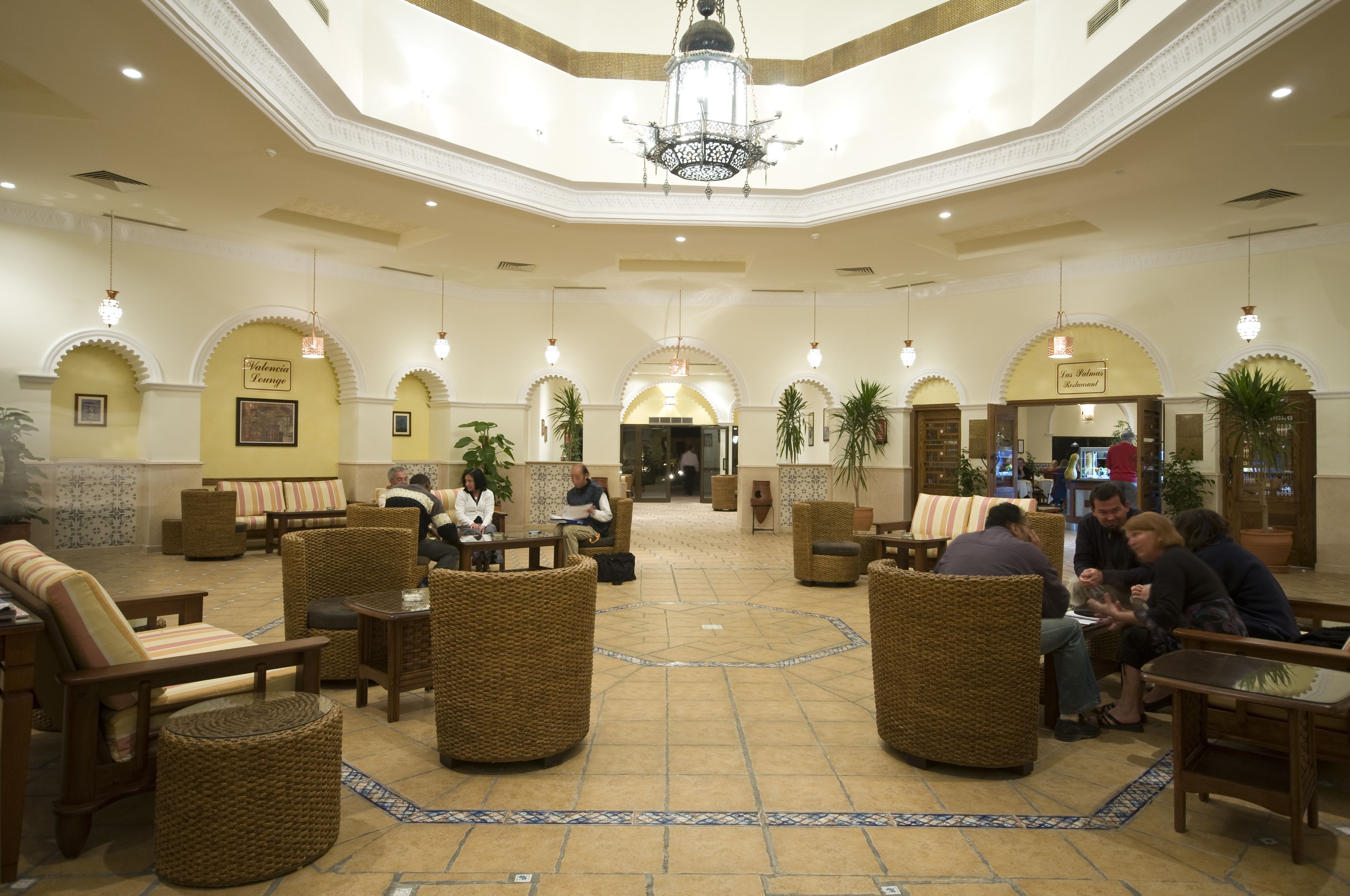 A spacious lobby with wicker furniture, a central chandelier, and arched doorways.