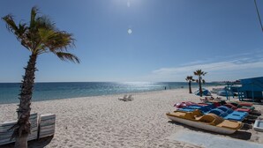 Une plage bordée d’une rangée de pédalos aux couleurs vives, un palmier et un ciel bleu azur.