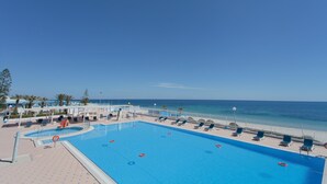 Une piscine avec des chaises longues et vue sur la plage.
