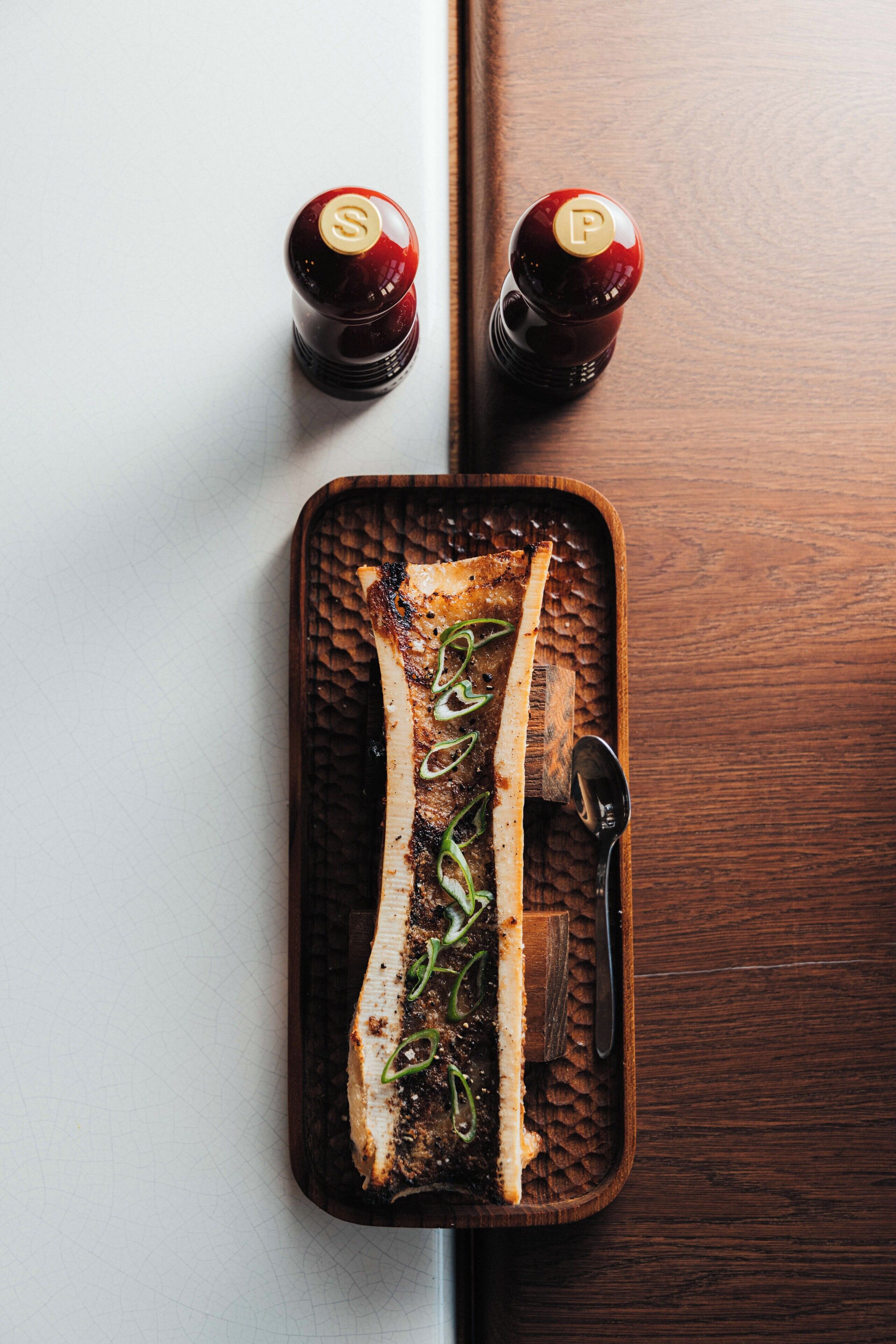 Ein hölzernes Tablett mit einem gekochten Fisch und einem Löffel auf einer Holztischplatte.