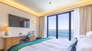 Een hotelkamer met een groot bed, een bureau, een stoel en uitzicht op de oceaan.