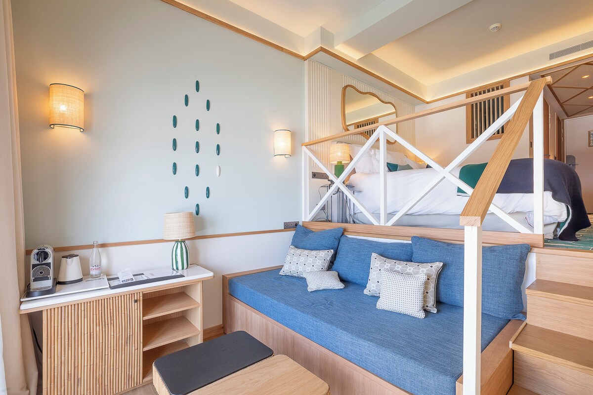 A modern room with a bunk bed, a sofa bed, a bedside table with a lamp, and a wall-mounted mirror.