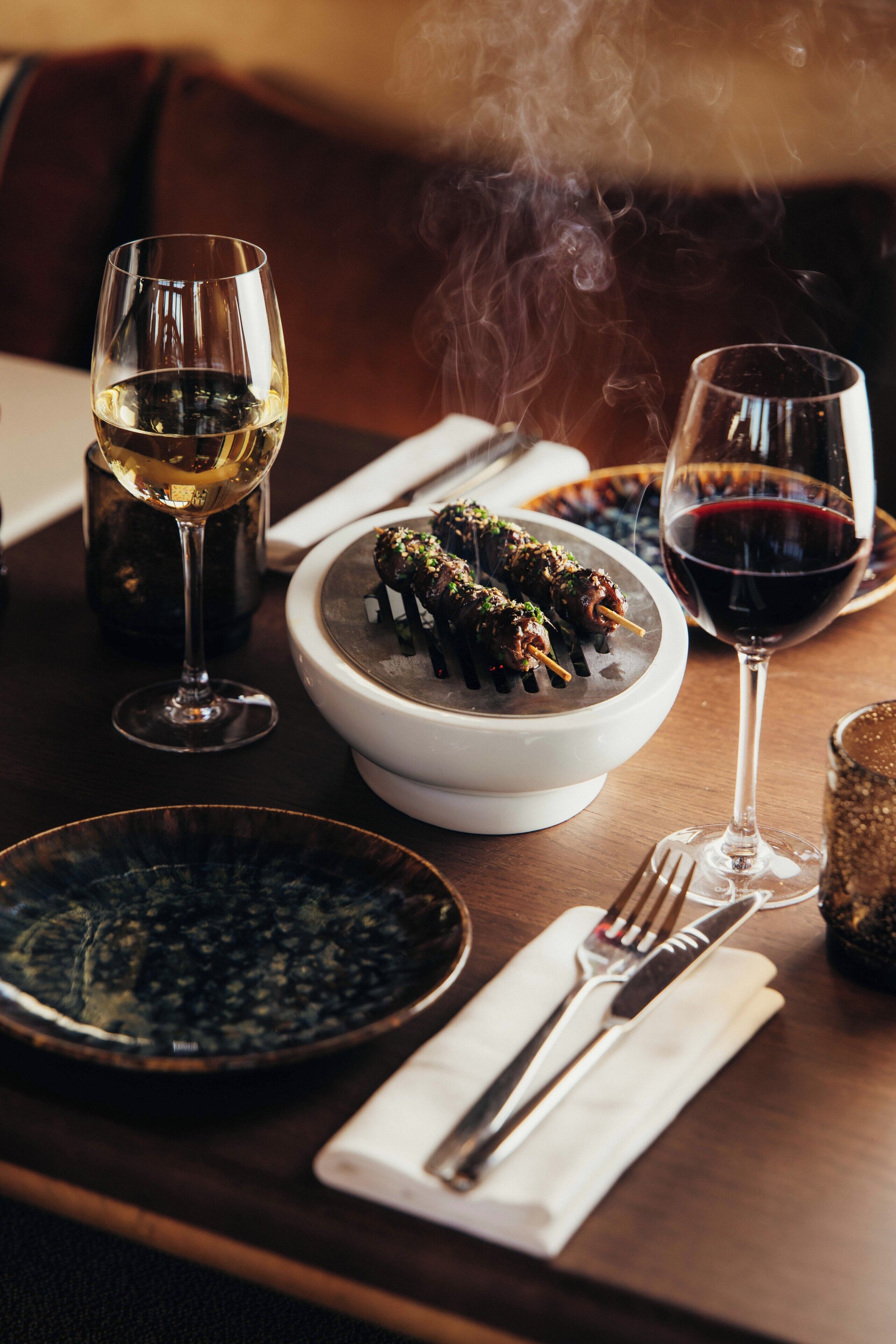 Una mesa de comedor con un bol de comida, dos copas de vino y un plato de comida.