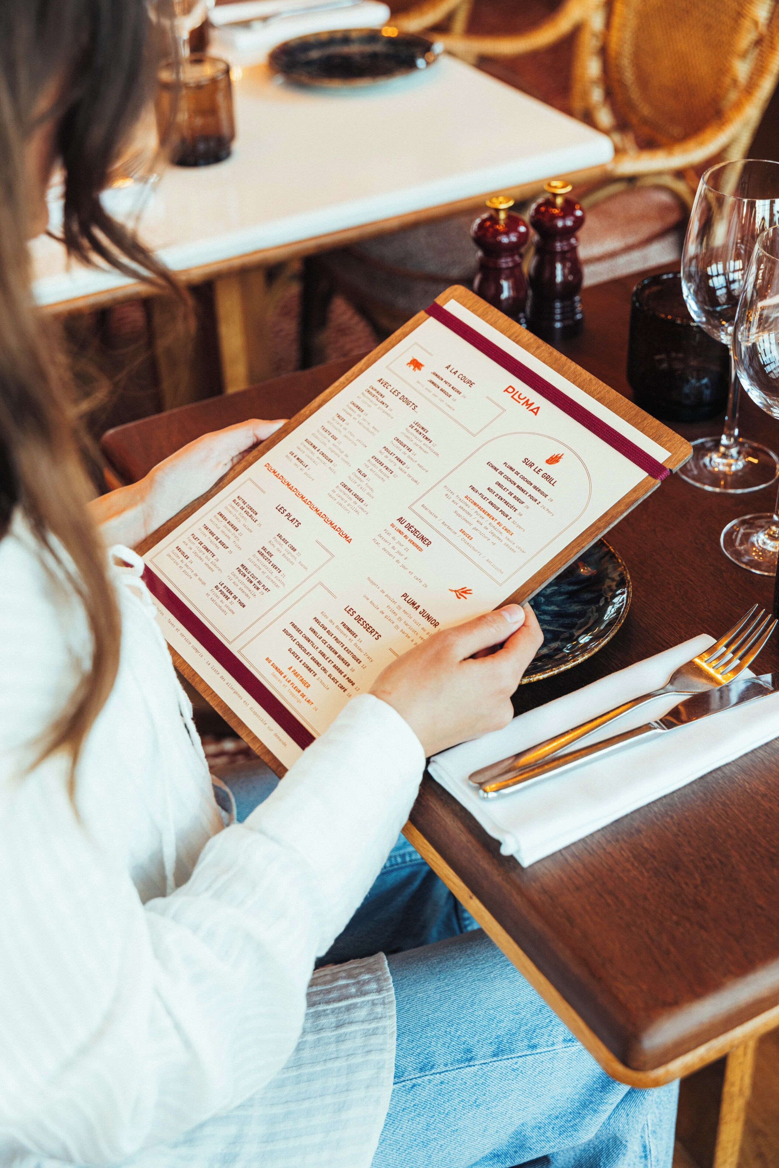 Une personne tenant un menu à une table de restaurant, avec une bougie, des salières et des poivrières, et un verre à vin.