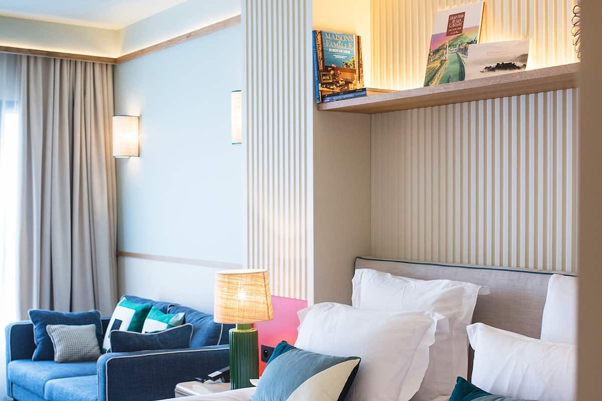 A hotel room with a large bed, a sofa, a lamp, and a view of the city through the window.