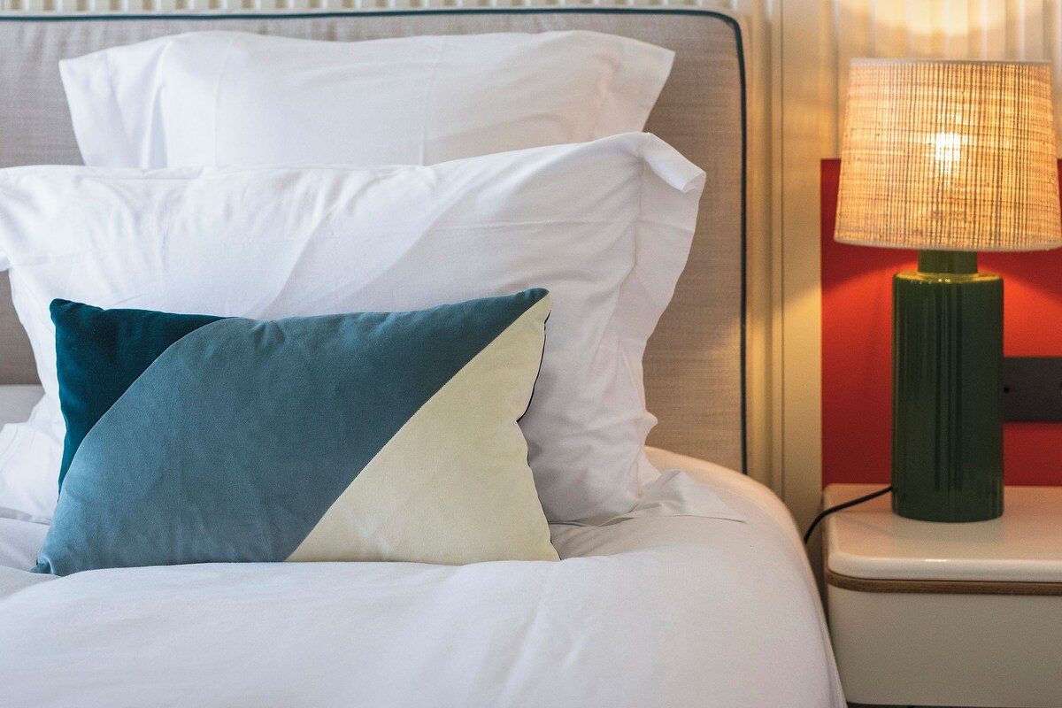 A neatly made bed with white and teal pillows, a green throw blanket, and a green lamp on a bedside table.