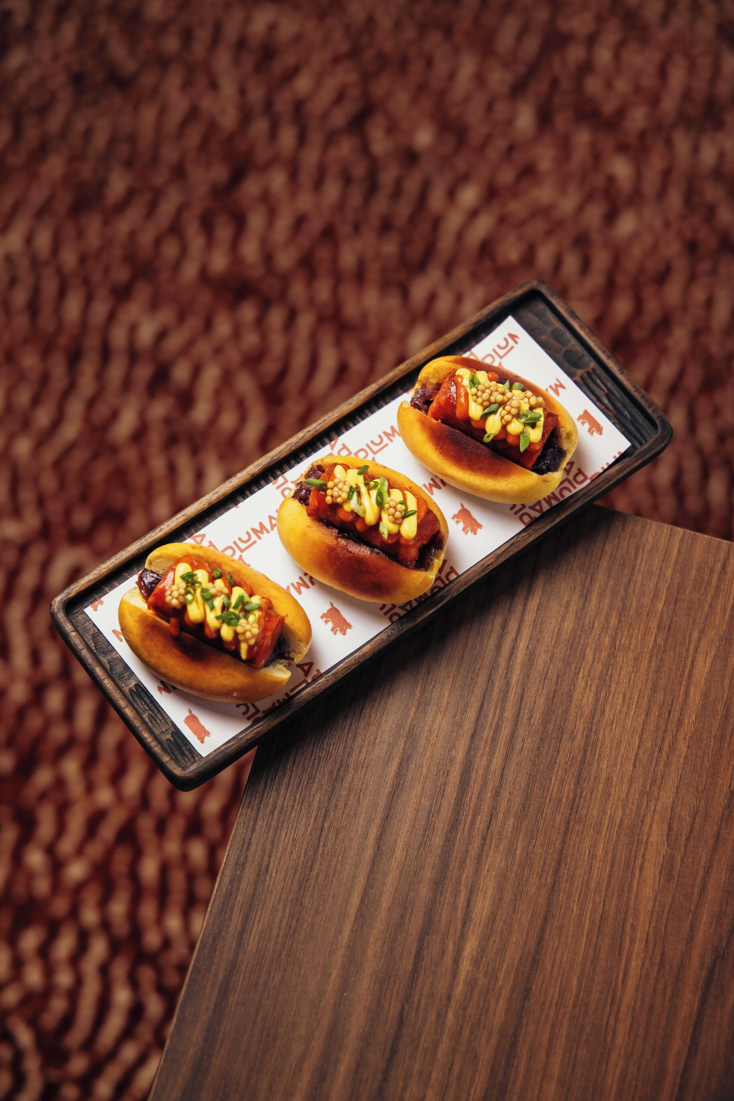 A tray with three hot dogs on a wooden surface.