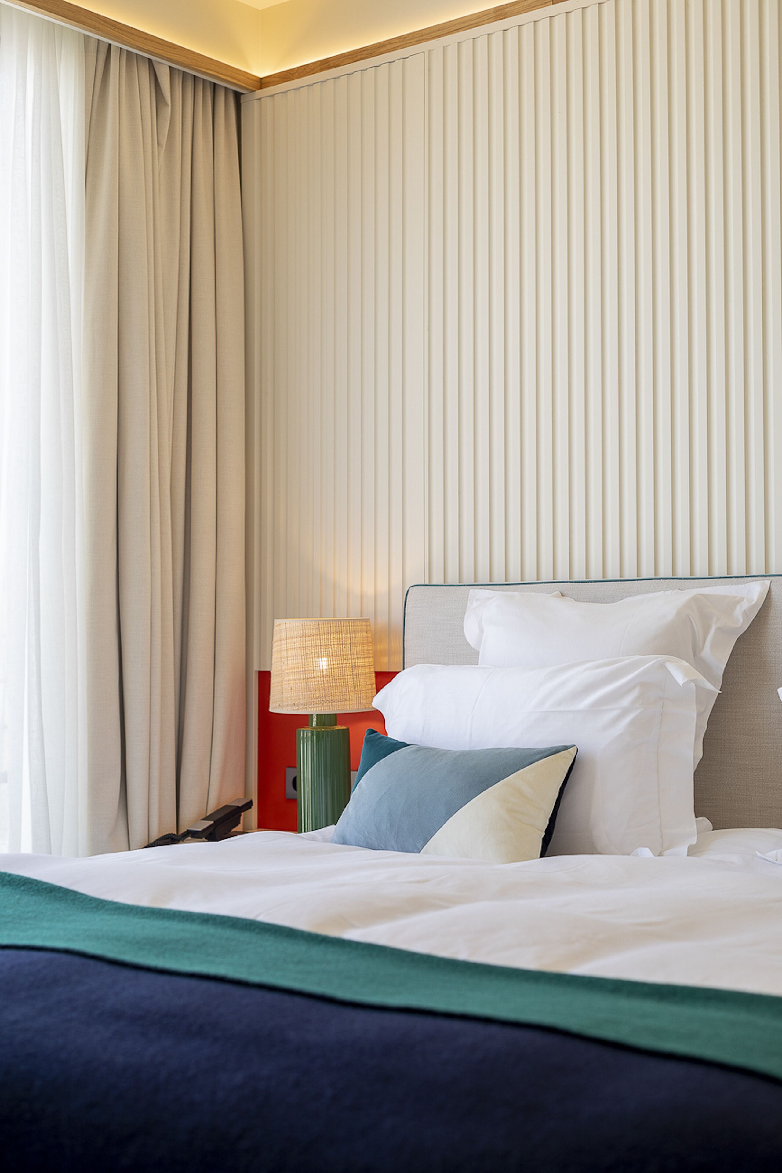 Una habitación de hotel con cama, cortinas, lámpara y mesita de noche.