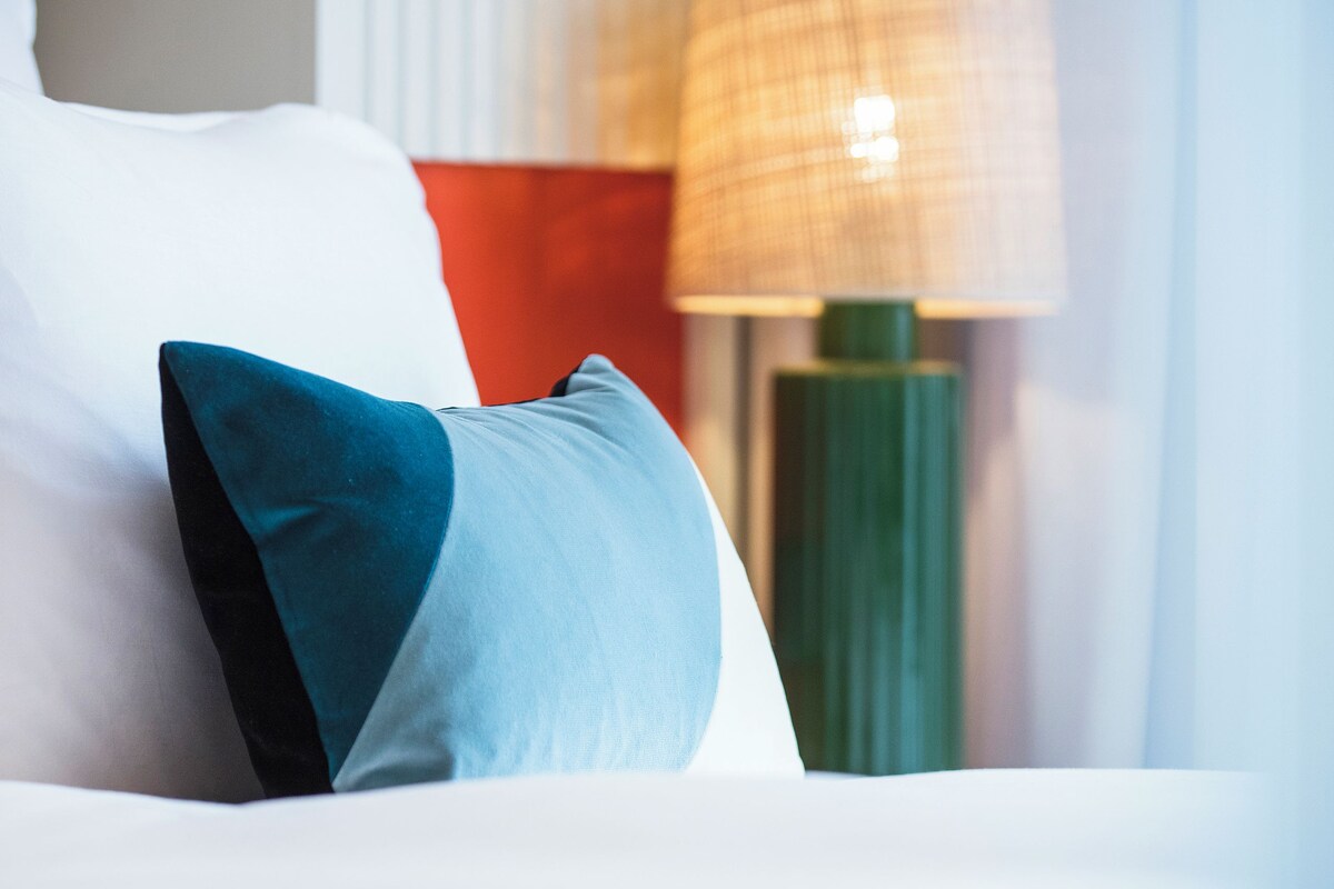 A neatly made bed with a blue pillow and a green lamp in the background.