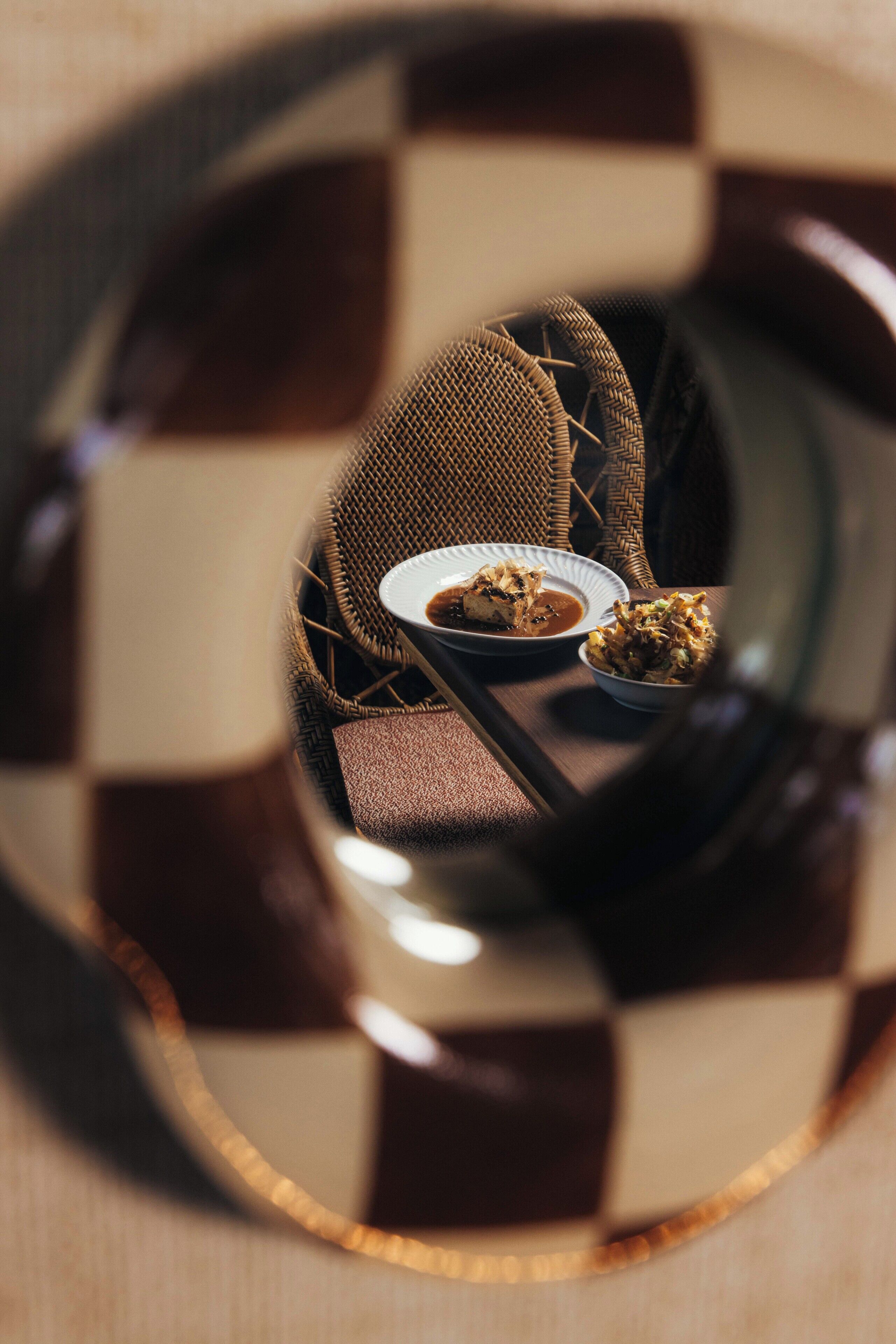 A checkered floor pattern, a woven chair, and a table with a plate of food.